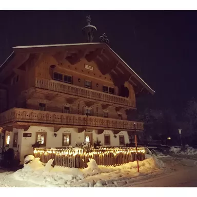 A cozy wooden house in a snowy landscape at night. It is decorated with lights and radiates an inviting atmosphere.