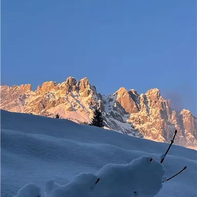 Schneebedeckte Berge im Sonnenlicht unter klarem blauen Himmel. Ein frostiger Vordergrund mit Schnee.