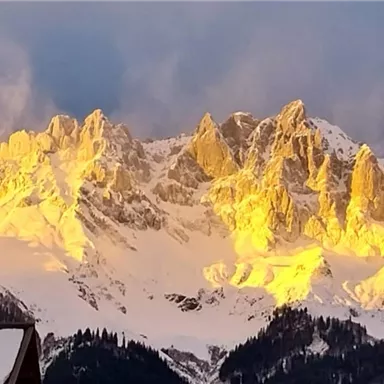 Ein beeindruckendes Bergpanorama mit schneebedeckten Gipfeln im warmen Licht der Abenddämmerung. Die Felsen strahlen in goldenen Tönen und schaffen eine malerische Atmosphäre.