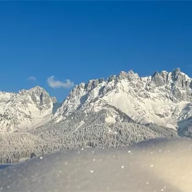 Eine beeindruckende Berglandschaft mit schneebedeckten Gipfeln unter einem klaren blauen Himmel. Im Vordergrund liegt eine sanfte Schneedecke.