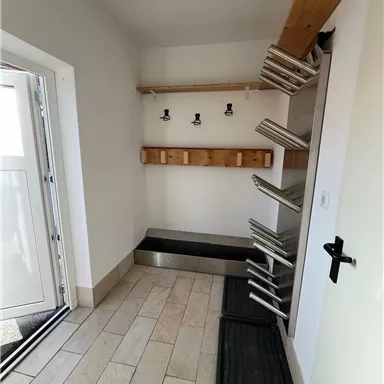 A practical entrance area with a coat hook and shoe shelves. The floor is tiled and the room feels bright and inviting.