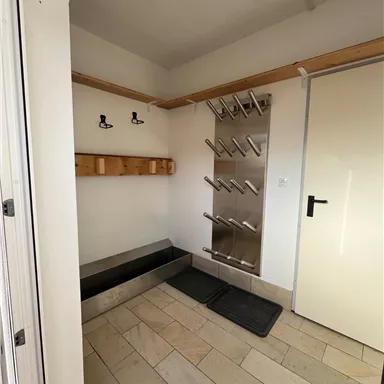 A functional entrance area with hooks and a rack for sports equipment. The walls are bright and the floor is made of light tiles.