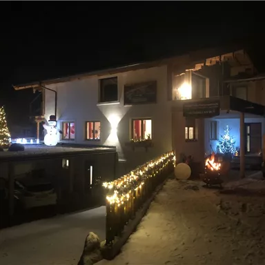 Ein schön dekoriertes Haus im Schnee bei Nacht. Lichter und ein Schneemann verleihen eine festliche Stimmung.