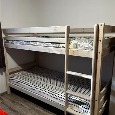 A bunk bed made of wood with an upper and a lower mattress. The room has a simple and modern style with a wooden floor.