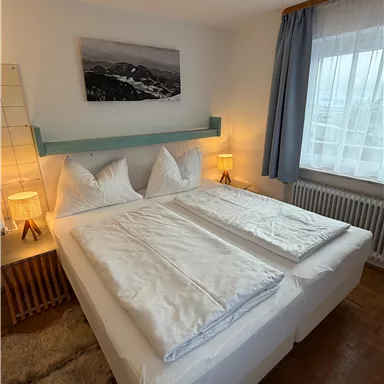 A cozy bedroom with a double bed and two nightstands. Large windows create plenty of daylight and a relaxed atmosphere.