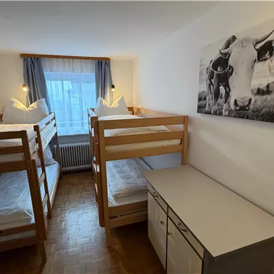 A simple room with two bunk beds and a desk. A picture of a cow is hanging on the wall.