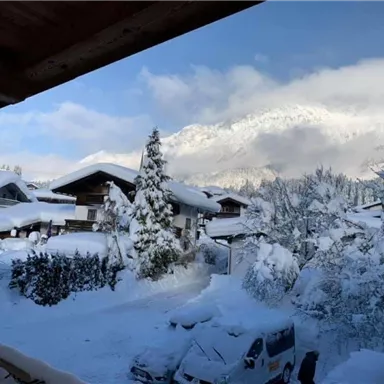 Zwei Reihen von verschneiten Häusern unter einem klaren blauen Himmel. Im Hintergrund sind majestätische Berge zu sehen.