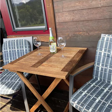 A small table with two chairs on a balcony. On the table are a bottle of wine and two glasses.