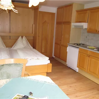 A cozy apartment with a double bed and a small kitchen. The wooden floor and warm colors create an inviting atmosphere.