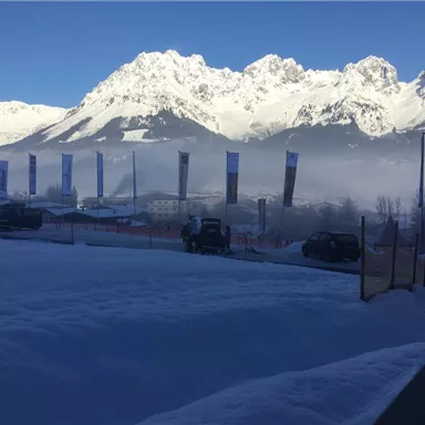 Eine verschneite Landschaft mit majestätischen Bergen im Hintergrund. Fahnen wehen im kalten Wind unter einem klaren blauen Himmel.