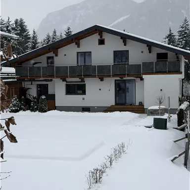 A modern house in a snowy landscape. The garden is covered with fresh snow and surrounded by trees.