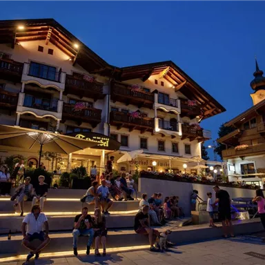 Eine malerische Stadt mit traditionellen Gebäuden und vielen Menschen, die am Abend entspannen. Die Umgebung ist schön beleuchtet und vermittelt eine lebhafte Atmosphäre.