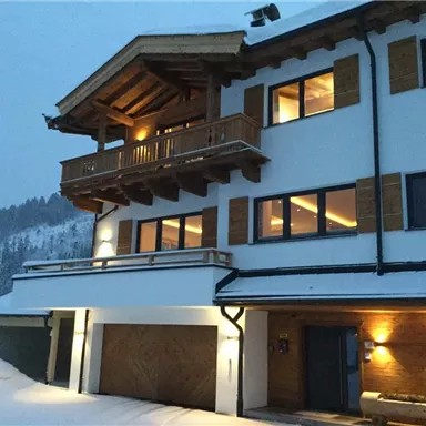 Ein modernes Chalet in den Bergen, umgeben von Schnee. Die warmen Lichter der Fenster schaffen eine gemütliche Atmosphäre.