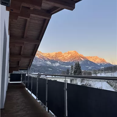 A terrace overlooking snow-capped mountains at sunset. The sky is clear and radiates in soft colors.