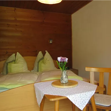 Ein gemütliches Schlafzimmer mit einem Doppelbett und zwei Kissen. Ein kleiner Tisch mit einer Vase und Blumen ergänzt die Einrichtung.