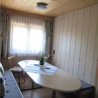 Ein gemütlicher Raum mit einem ovalen Tisch und Stühlen. Das Fenster lässt viel Tageslicht herein.