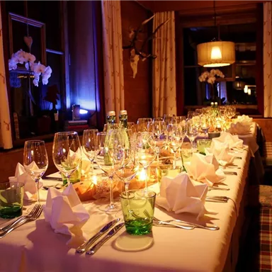 Ein festlich gedeckter Tisch in einem gemütlichen Raum. Die Tischdeko umfasst Gläser, Servietten und Kerzen für eine einladende Atmosphäre.