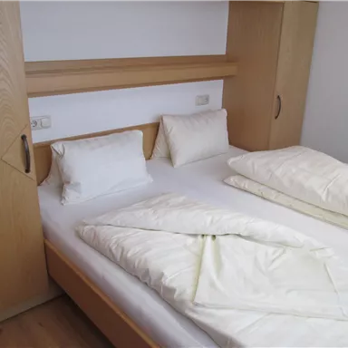 A simple bedroom with a double bed and two pillows. The furniture is made of light wood and the room feels clean and tidy.