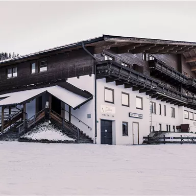 Ein gemütliches Gebäude im Schnee mit einem klassischen alpinen Design. Umgeben von schneebedeckten Bäumen und Bergen.