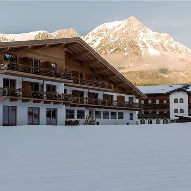Ein gemütliches Hotel im Schnee mit Blick auf die Berge. Die Fassade ist aus Holz und bietet Balkone mit Blick auf die winterliche Landschaft.
