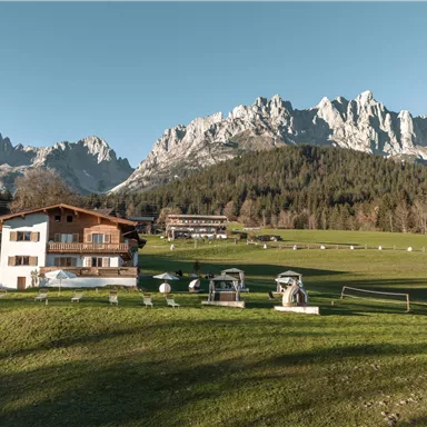 Ein malerischer Bauernhof in der Natur, umgeben von hohen Bergen. Der Himmel ist klar und die Landschaft wirkt friedlich.