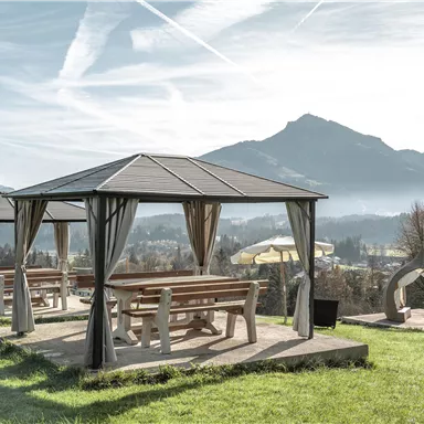 Ein schöner Ausblick auf eine grüne Wiese mit pavillonartigen Unterständen. Im Hintergrund sind Berge und der klare Himmel zu sehen.