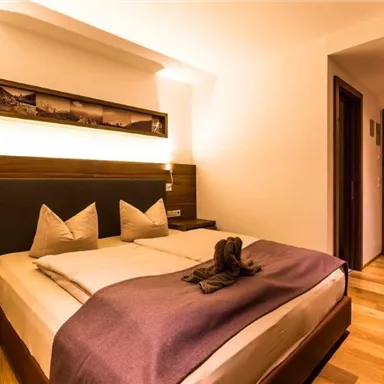 Ein gemütliches Schlafzimmer mit einem großen Bett und Holzfußboden. Die warmen Farben und sanfte Beleuchtung schaffen eine einladende Atmosphäre.