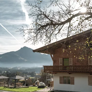 Ein charmantes Holzhaus steht vor einem beeindruckenden Bergpanorama. Der Himmel ist klar mit einigen Wolkenstreifen und die Landschaft ist friedlich.