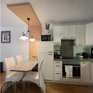 A modern kitchen with white furniture and a dining table. The room is bright and welcoming, ideal for cozy moments.