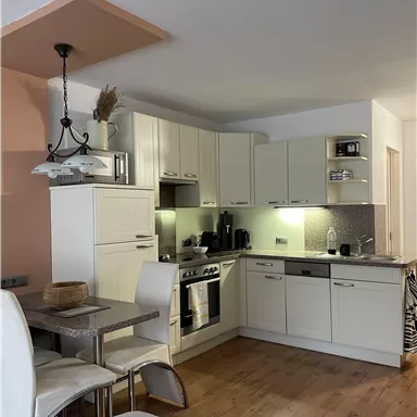A modern kitchen with white cabinets and stainless steel appliances. Next to it is a dining area with a small table and chairs.
