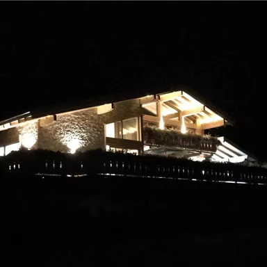 Ein modernes Holzhaus, das in der Nacht beleuchtet ist. Der lichtdurchflutete Balkon und die warmen Lichter schaffen eine gemütliche Atmosphäre.