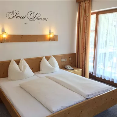 Ein gemütliches Schlafzimmer mit einem Doppelbett und zwei Kissen. Das Zimmer hat große Fenster und eine warme Holzverkleidung.