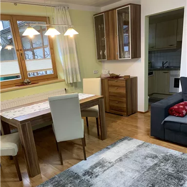 Ein gemütliches Wohn-Esszimmer mit einem Holztisch und modernen Stühlen. Der Raum ist hell und freundlich, mit einem Sofa und einem Teppich.