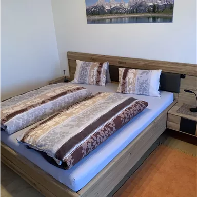 Ein gemütliches Schlafzimmer mit einem Doppelbett und warmen Farben. An der Wand hängt ein Bild von Bergen und Wasser.