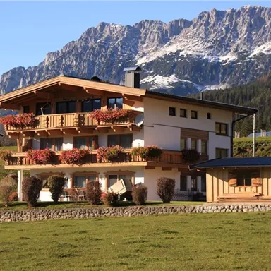 Ein schönes Haus in der Natur mit bunten Blumen auf dem Balkon. Im Hintergrund erheben sich majestätische Berge.