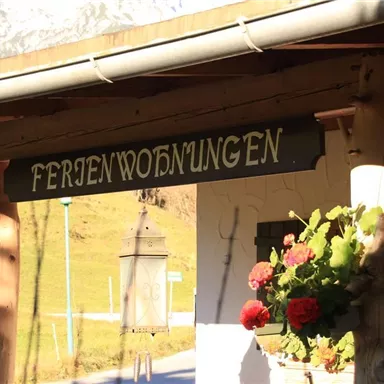 Ein einladendes Ferienwohnungsportal mit blühenden Pflanzen. Der Schriftzug „Ferienwohnungen“ ist gut sichtbar über dem Eingang platziert.