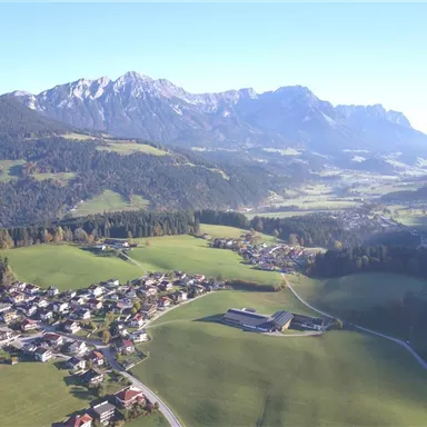 Eine malerische Landschaft mit sanften Hügeln und kleinen Dörfern. Im Hintergrund erheben sich majestätische Berge unter klarem Himmel.