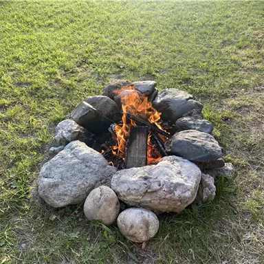 A campfire in a stone circle on green space. The fire burns brightly and creates a warm atmosphere.