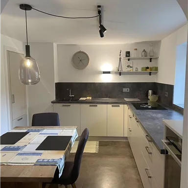 Eine moderne Küche mit hellem Design und einer Holz-Essgruppe. Sie umfasst eine Arbeitsfläche, Schränke und eine elegante Pendelleuchte.