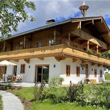 Ein schönes Landhaus mit Holzbalustraden und einem großen Balkon. Der Garten ist grün und lädt zum Entspannen ein.
