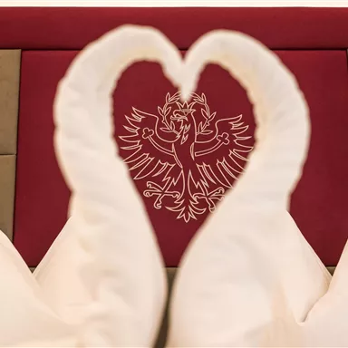 Ein romantisches Arrangement aus Handtüchern in Form von Schwänen. Im Hintergrund ist ein dekoratives Wappen zu sehen.
