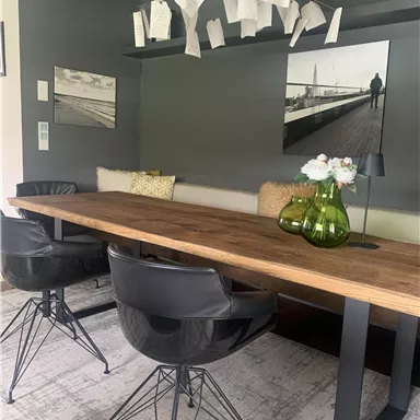 A modern dining area with a large wooden table and black chairs. Papers hang from the ceiling, and decorative vases with flowers are on the table.