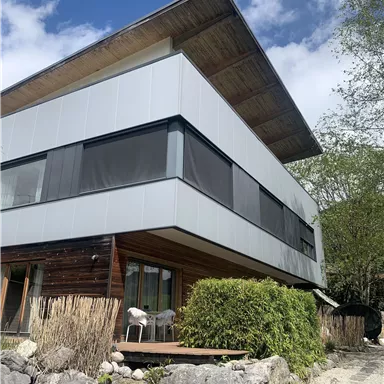 A modern residential building with a combination of wood and metal façade. Surrounded by green vegetation and stone ground.