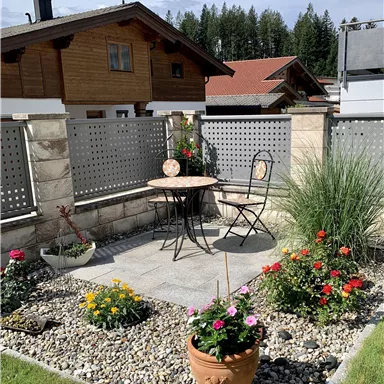 A beautiful garden area with a table and a chair. Colorful flowers and a paved floor create an inviting atmosphere.