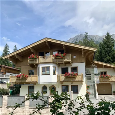 A beautiful chalet with balconies adorned with blooming plants. In the background, mountains and a clear sky can be seen.