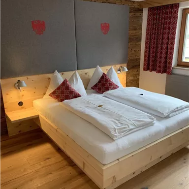 A cozy bedroom with a large bed, red decor, and wooden flooring. The walls are painted in neutral colors, creating an inviting atmosphere.