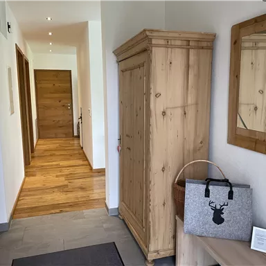 Ein heller Flur mit Holzfußboden und Wänden. Auf der linken Seite steht ein Holzschrank und ein dekorativer Spiegel ist an der Wand.