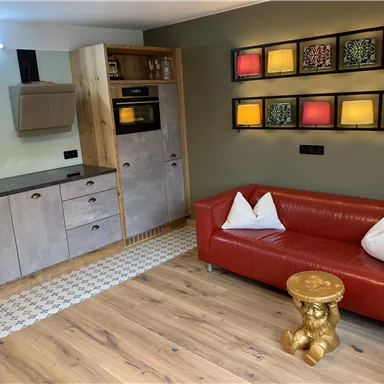 A modern kitchen with wood and metal details. A red sofa with white cushions and a gold side table complete the room.