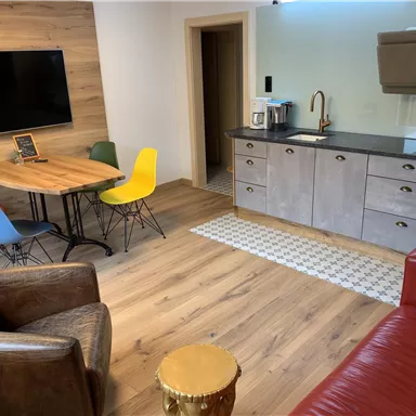 A modern room with a dining area and a kitchenette. Colorful chairs around the table and a cozy sofa create an inviting atmosphere.