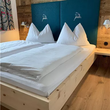 A cozy bedroom with a double bed and white pillows. The walls are made of wood, and there is soft lighting.